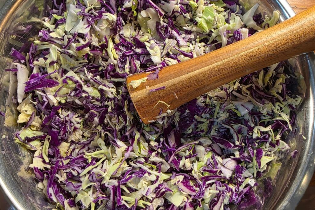 mixing cabbage in a bowl to make sauerkraut
